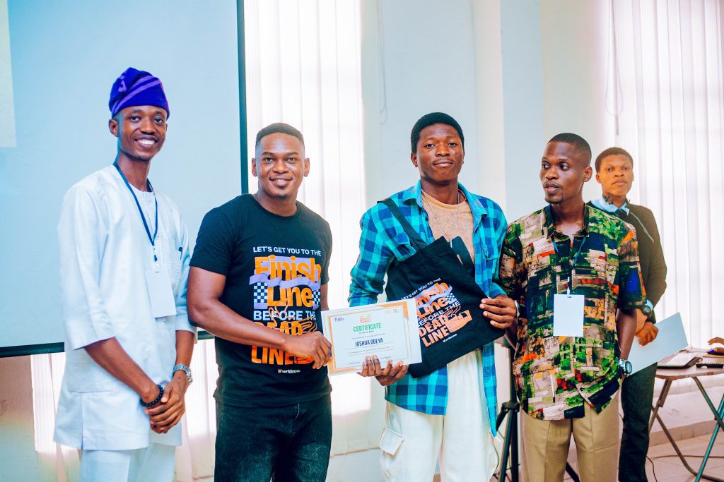 Joshua Obeya, second place winner of the 2026 Chidera Anushiem Undergraduate Essay Competition receiving his award at the 2026 Ibadan Boys Conference, flanked by BWB NG co-founders and a representative of partner organization, Writinova